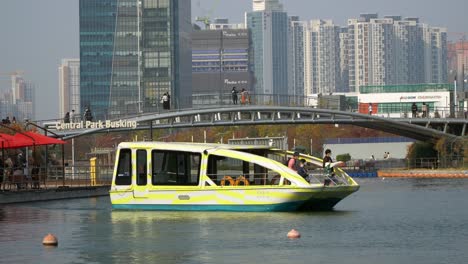 Songdo-Central-Park---People-in-masks-sightseeing-urban-Incheon-city-skyline-from-a-water-taxi-on-lake-and-footbridge-across-the-water