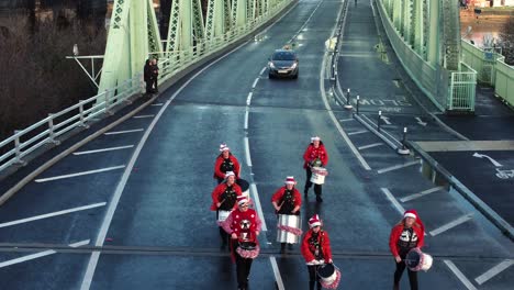 Charity-Santa-dash-funny-musical-marching-drummer-band-Runcorn-Silver-Jubilee-bridge-Aerial-view-tracking-reverse