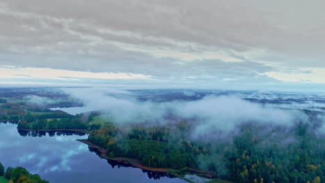 aerial-reversing-flight-over-lush-autumn-forest-and-lake-landscape,-in-cloudy-daytime