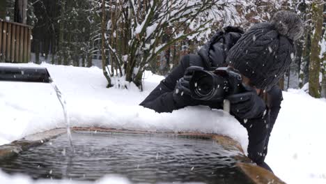 Woman-taking-photos-of-flowing-water-during-winter-season-and-snowfall
