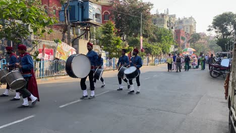 Static-view-of-a-youth-band-wearing-blue-costume-and-marching-while-playing-musical-instruments-on-the-road-followed-by-TMC-party-procession-with-banners-ahead-of-Kolkata-civic-polls