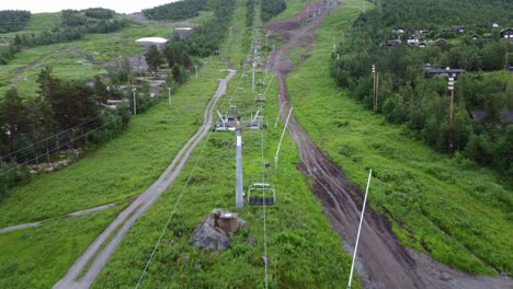 Ski-lift-not-in-use-during-summer-at-Ski-Geilo-Norway---Forward-moving-aerial-above-ski-lift-and-muddy-trail