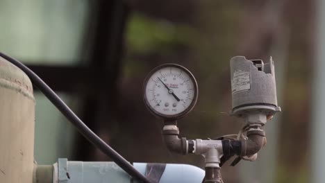 Close-up-shot-of-a-pressure-gauge-on-an-outdoor-water-system,-the-tank-providing-a-constant-flow-of-water-as-part-of-the-plumbing-and-irrigation-on-a-floating-riverboat,-Kanchanaburi,-Thailand