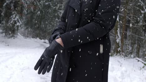 Woman-putting-on-warm-gloves-on-cold-winter-day-in-forestry-area-while-snowing