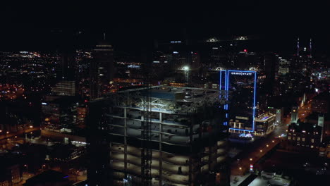 Night-aerial-of-building-tower-under-construction-with-cranes-on-top,-Drone-4K