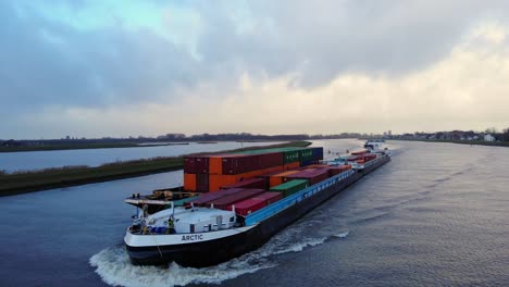 Luftaufnahme-Des-Hafenbugs-Eines-Kreisförmigen-Binnencontainerschiffs,-Das-Entlang-Des-Flusses-Noord-Fährt