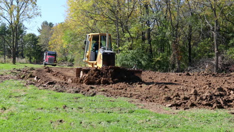 Small-bulldozer-pushing-soil-for-site-preparation-for-new-barn-construction-in-early-autumn