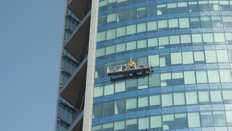 Close-up-of-a-window-cleaner-hanging-from-a-glass-curtain-wall-of-modern-skyscraper-at-daytime,-Santiago-Chile