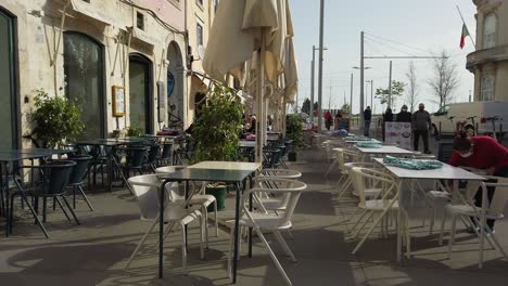 Blick-Auf-Leere-Tische-Und-Stühle-Vor-Dem-Restaurant-In-Lissabon,-Während-Der-Wind-Auf-Sonnenschirmen-Weht