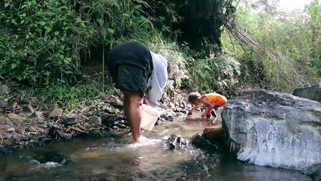 Mother-and-her-small-daughter-at-a-small-creek-clearing-stones-for-good-water-flow