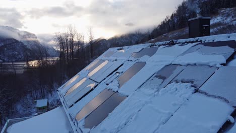 Paneles-Solares-En-Una-Casa-Privada-Cubierta-De-Nieve---Humo-De-La-Chimenea-Con-Un-Impresionante-Fondo-De-Paisaje-De-Fiordos---Hermosos-Reflejos-Del-Amanecer-En-Paneles-Solares---Noruega