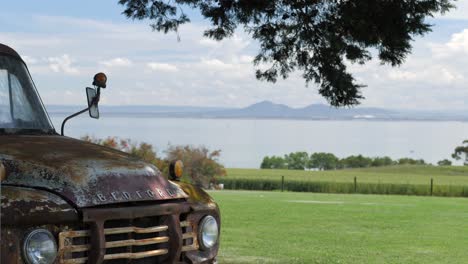 Old-Rusted-Truck-Idle-Near-Green-Fields-And-Ocean-Scene,-SLOW-MOTION