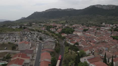 Tracking-aerial-follows-red-train-through-small-French-Pyrenees-town