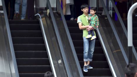 Zeitlupen-Nahaufnahme-Eines-Asiatischen-Vaters-Mit-Seinem-Kleinen-Kind,-Das-Auf-Einer-Rolltreppe-Steht