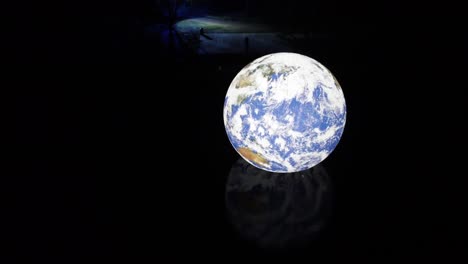 Luke-Jarram-Schwimmende-Erde,-Beleuchteter-Planet,-Der-Sich-Im-Seewasser-Spiegelt-Und-Sich-Nachts-Auf-Der-Kräuselnden-Oberfläche-Zurückzieht