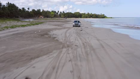 Aerial-backwards-shot-of-Mini-Cooper-driving-on-sandy-beach-beside-Caribbean-Sea-on-Dominican-Republic---Tracking-shot-for-commercial-tv