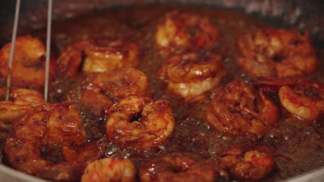 Delicious-seafood-cooking-scene-with-chef-using-tongs-to-flip-the-prawns,-coating-shrimps-with-sweet-paprika-sauce,-simmering-on-hot-shallow-frying-pan,-close-up-shot