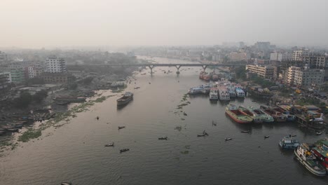 River-through-city-with-bridge-and-cargo-ships---aerial-establishing-drone-pull-back-shot