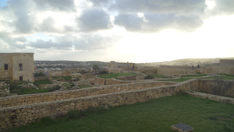 Greenery-and-Ruins-inside-of-Cittadella-Fortress-with-Sun-Setting-Down-and-People-Walking-Around