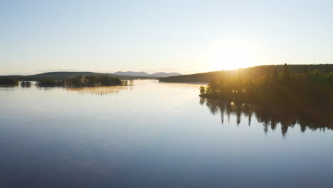 Luftflug-über-Einem-Nebligen-See-Bei-Sonnenaufgang-Mit-Inseln-Mit-Grünen-Bäumen-Und-Bergen-Im-Hintergrund,-Gefilmt-In-Lappland,-Finnland