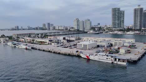 Küstenwachestation-Mit-Am-Pier-Angedockten-Schnellbooten-Der-Küstenwache-|-Videohintergrund-Der-Stadt-Miami-Mit-Modernen-Architekturgebäuden,-Einer-Stadt-In-Der-Nähe-Einer-Bucht,-Luftaufnahme-In-4K