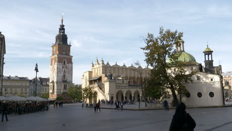 People-Strolling-At-The-Main-Market-Square-Of-Krakow-In-Poland-With-View-Of-Town-Hall-Tower,-Cloth-Hall,-And-Church-Of-St