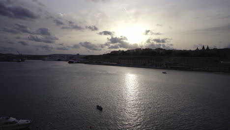 Silhouetted-landscape-at-sunset-on-Valletta-coast,-boats-passing-by