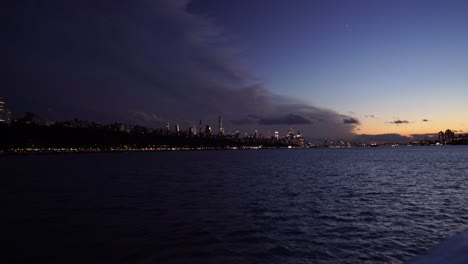 Sunset-skyline-of-New-York-City-modern-cityscape-illuminated-at-dusk,-boat-approaching-the-city-center-during-sunset