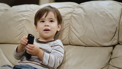 Asian-two-years-old-kid-watches-TV,-holds-a-remote-control-in-his-hands
