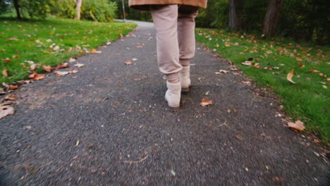 A-woman-walks-along-a-path-in-an-autumn-park,-only-her-legs-are-visible-in-the-frame.