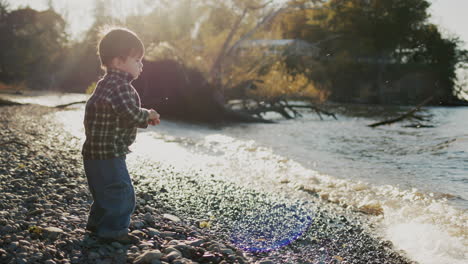 A-little-Asian-boy-plays-on-the-shore-of-a-lake,-throws-pebbles-into-the-water
