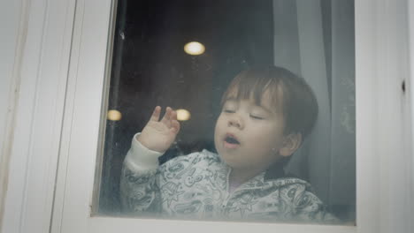 A-little-boy-looks-out-the-window,-reacts-emotionally-and-cheerfully-to-what-he-saw.-Multi-ethnic-Child-of-two-years