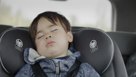 Trip-with-a-child---a-multi-ethnic-two-year-old-boy-naps-in-a-car-seat-in-the-back-seat-of-a-car