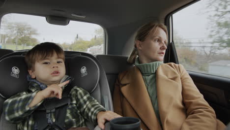 Eine-Frau-Mit-Einem-Zweijährigen-Kind-Fährt-Auf-Dem-Rücksitz-Eines-Autos,-Ein-Baby-Sitzt-In-Einem-Autositz