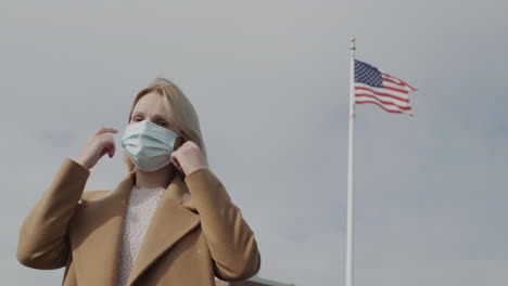 Porträt-Einer-Frau-In-Einer-Schutzmaske-Vor-Dem-Hintergrund-Der-Amerikanischen-Flagge.-4K-Video
