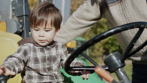 Baby-farmer-playing-behind-the-wheel-of-a-tractor,-next-to-his-father