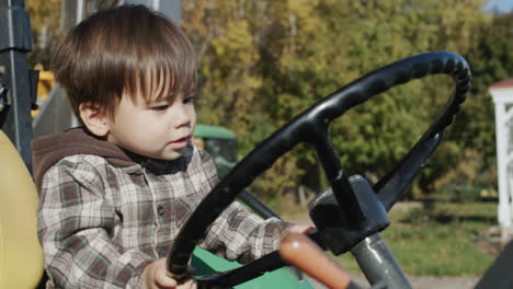 Asian-kid-playing-tractor-driver,-sitting-behind-the-wheel-of-a-tractor.