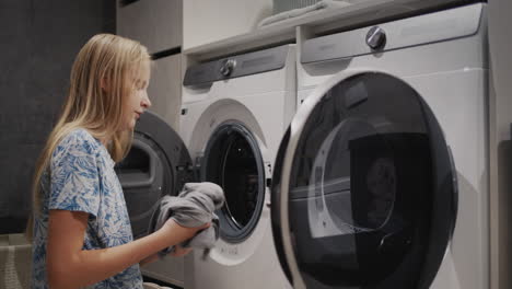Ein-Junges-Mädchen-Legt-Saubere-Kleidung-Von-Der-Waschmaschine-In-Den-Trockner
