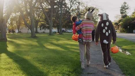 Mom-with-two-children-in-carnival-costumes-in-honor-of-Halloween.-Walking-down-the-street-of-a-small-American-town