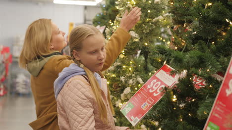 A-woman-with-a-child-chooses-a-Christmas-tree-in-the-store.-Shopping-before-the-winter-holidays