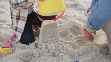 Hands,-family-and-child-with-sand-castle-at-beach