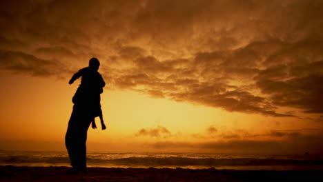 Sunset,-father-and-lifting-a-kid-in-air-at-beach