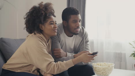 Junges-Afroamerikanisches-Paar-Wählt-Mit-Der-Fernbedienung-Etwas-Aus,-Das-Es-Im-Fernsehen-Sehen-Möchte