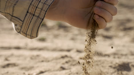 Nahaufnahme-Der-Hand-Eines-Mannes,-Der-Auf-Dem-Land-Sand-Vom-Boden-Aufsammelt