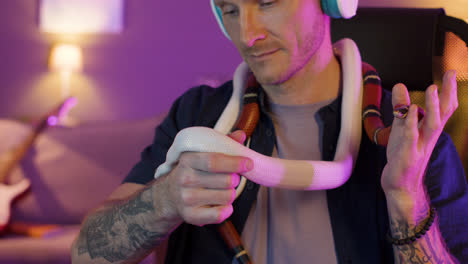 Close-up-view-of-caucasian-man-in-headphones-sitting-at-desk-while-petting-and-holding-two-snakes-around-his-neck