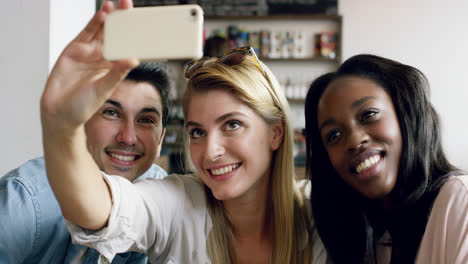 Grupo-Diverso-De-Amigos-Tomando-Autorretrato-Selfie-En-La-Cafetería-Usando-Un-Teléfono-Inteligente