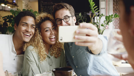 Mixed-race-group-of-friends-taking-selfie-photograph-in-cafe