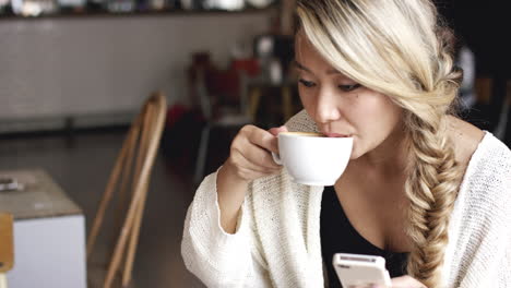 Mujer-Asiática-Comprando-Un-Teléfono-Inteligente-En-Línea-En-Una-Cafetería-Tomando-Café