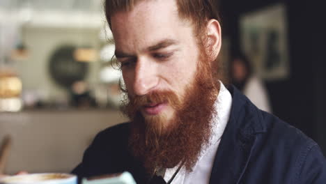 Man-using-mobile-phone-in-cafe-is-happy-hipster