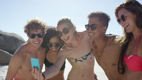 Mixed-race-group-of-friends-taking-selfies-on-the-beach-using-phone-camera